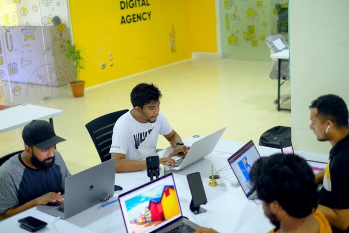 Pria berbaju polo putih duduk di kursi menggunakan MacBook